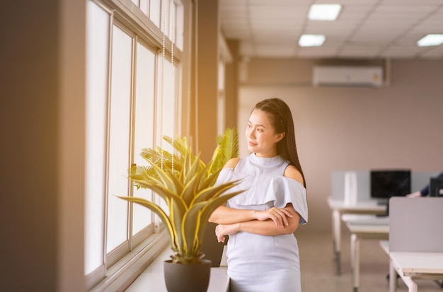 Hermosa mujer asiática de negocios de pie y mirando por la ventana en la oficina