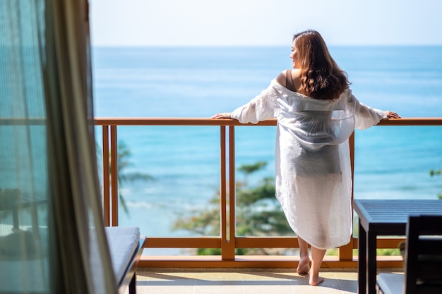 Foto una hermosa mujer asiática de pie y disfrutar viendo la vista al mar en el balcón