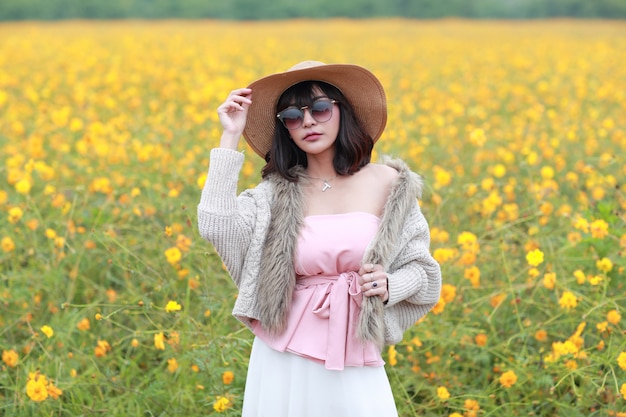 Hermosa mujer asiática de pie en la naturaleza entre campos de flores cosmos y mirando con tranquilidad