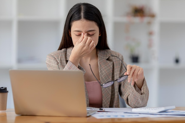 Hermosa mujer asiática que trabaja en una oficina, es una mujer de negocios propietaria de una empresa, tiene dolor de cabeza debido al papeleo largo y grande que la deja cansada y mareada El concepto de enfermedad del trabajo