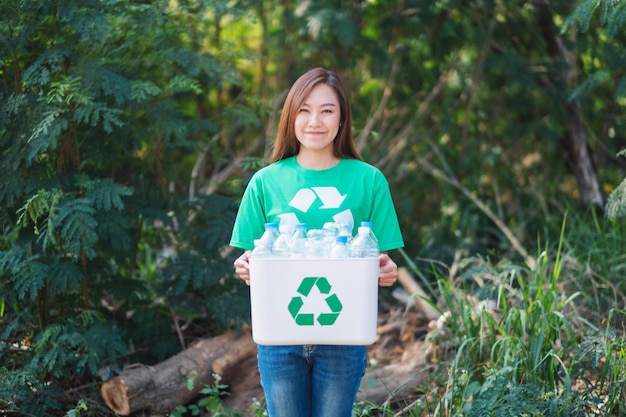 Una hermosa mujer asiática recogiendo basura y sosteniendo una papelera de reciclaje con botellas de plástico al aire libre