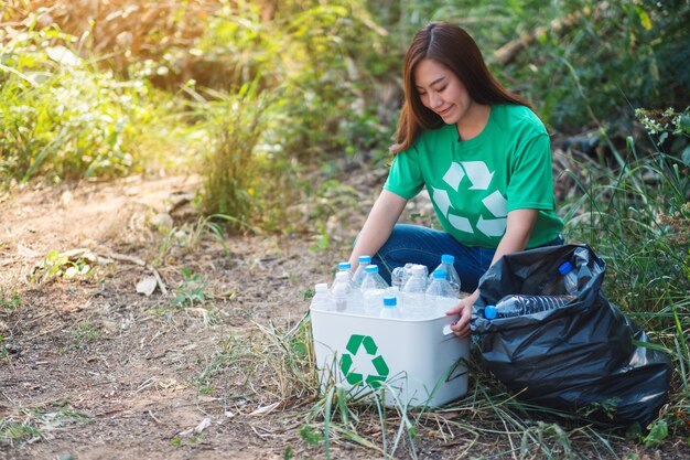 Una hermosa mujer asiática recogiendo botellas de plástico de basura en una caja y una bolsa para el concepto de reciclaje