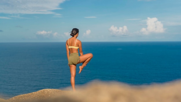 Hermosa mujer asiática en ropa deportiva haciendo yoga en el pico de la montaña junto al mar después del trekking