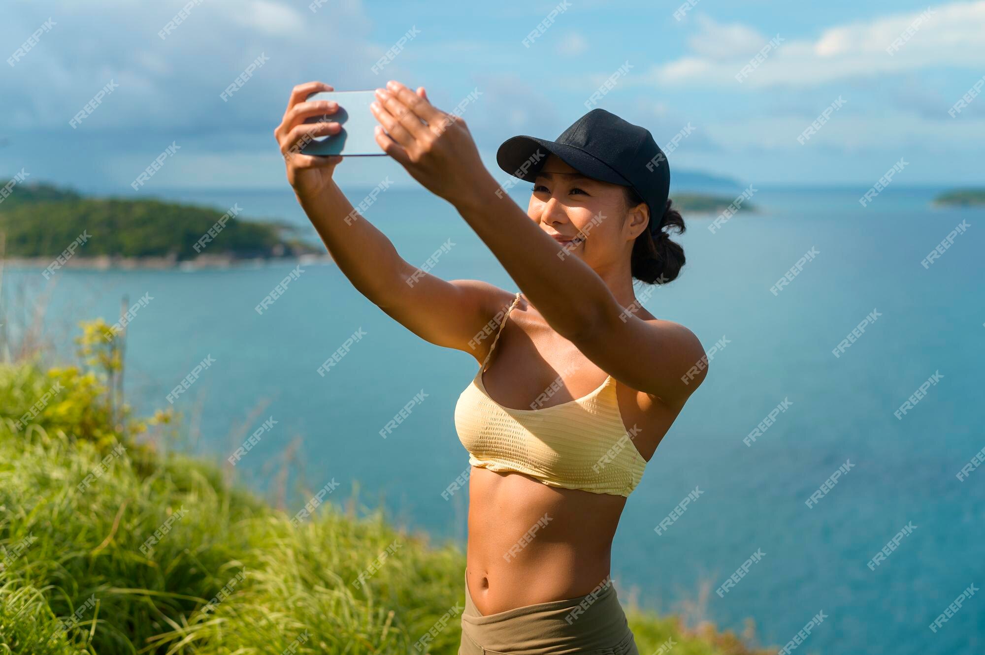 Hermosa mujer asiática en deportiva fotos en el pico de montaña junto al mar después del trekking | Foto Premium