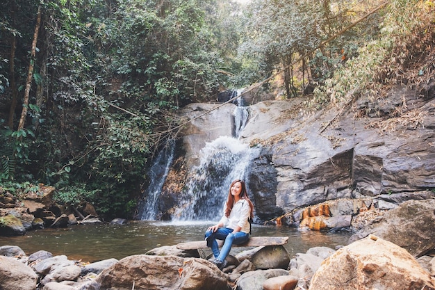 Una hermosa mujer asiática sentada frente a una cascada en la selva
