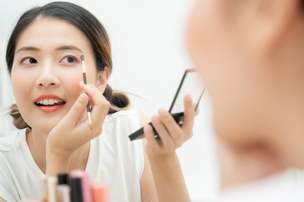 Hermosa mujer asiática sentada frente a un espejo y sonriendo en la cara maquillada de una mujer sana aplicando maquillaje Publicidad estilo de vida cosméticos accesorios de maquillaje actividad de belleza esteticista