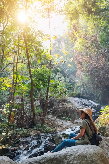 Una hermosa mujer asiática sentada sobre la roca frente a la cascada