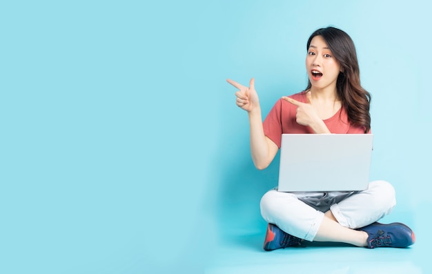 Hermosa mujer asiática sentada usando laptop y apuntando hacia los lados