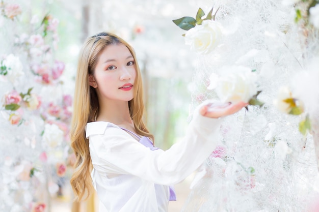 Hermosa mujer asiática sonríe y se para en el jardín de flores de rosas blancas como tema natural y de lujo