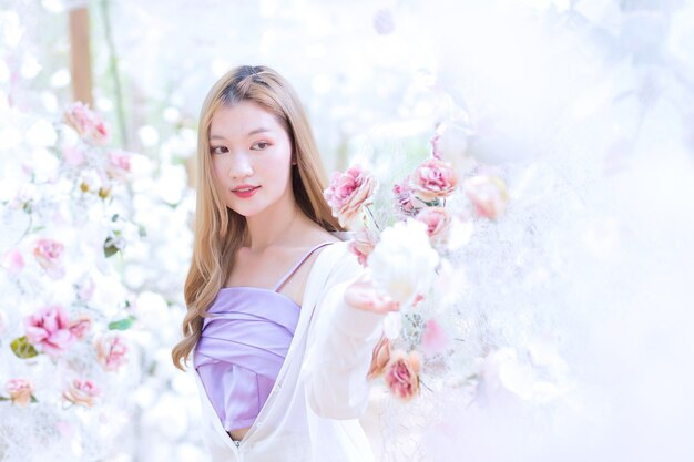 Hermosa mujer asiática sonríe y se para en el jardín de flores de rosas blancas como tema natural y de lujo