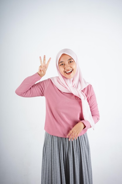 Hermosa mujer asiática sonriente con camiseta rosa y hiyab que aparece y señala hacia arriba