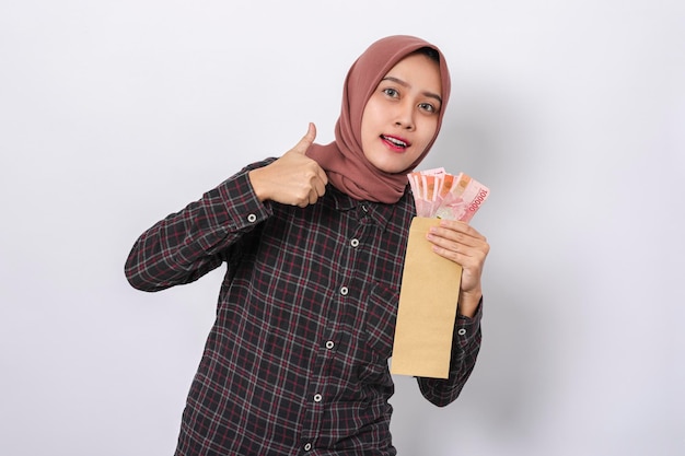 Foto hermosa mujer asiática sonriente con hiyab y camisa de franela con dinero en rupias indonesias