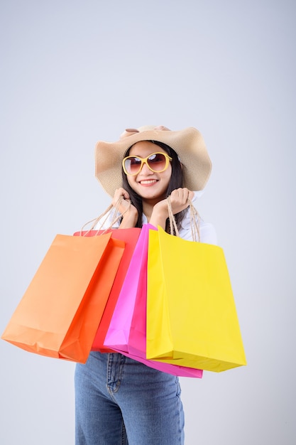 hermosa mujer asiática sosteniendo una bolsa de compras multicolor con una expresión feliz sobre fondo blanco.