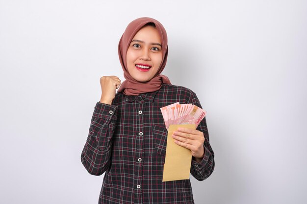 Foto hermosa mujer asiática sosteniendo dinero en rupias indonesias mientras hace el gesto de victoria