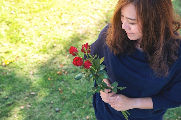 Una hermosa mujer asiática sosteniendo flores rosas rojas en un jardín verde con sentirse feliz en el día de San Valentín