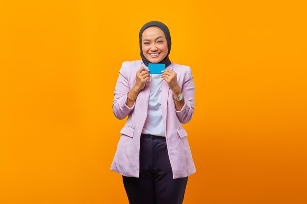 Hermosa mujer asiática sosteniendo en la mano tarjeta en blanco con cara sonriente sobre fondo amarillo