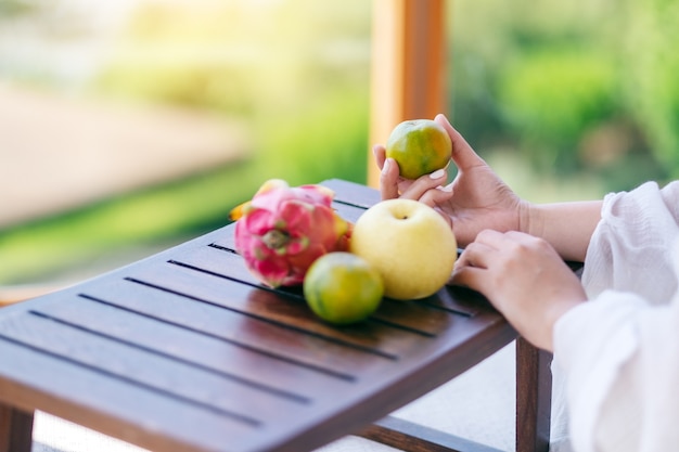 Una hermosa mujer asiática sosteniendo una naranja con pera y fruta del dragón en una pequeña mesa de madera