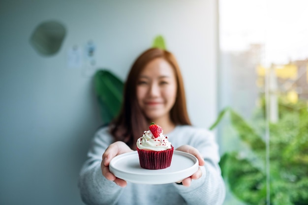 Una hermosa mujer asiática sosteniendo un plato de cupcake de terciopelo rojo