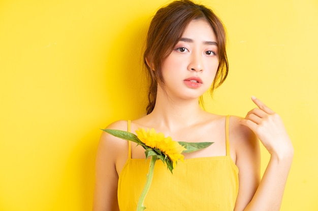 Hermosa mujer asiática sosteniendo y posando con girasol en amarillo