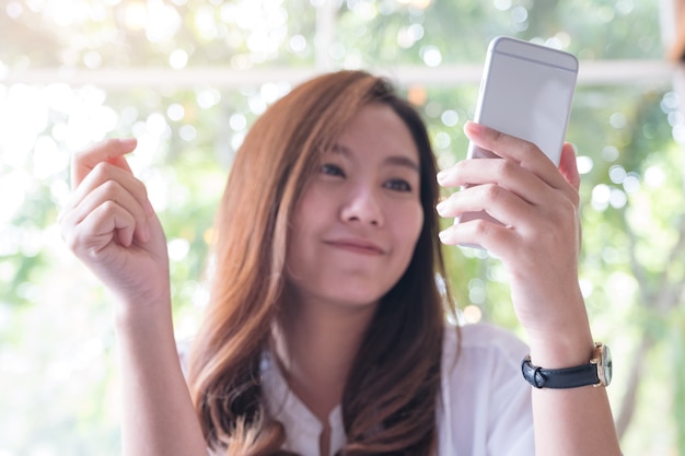 una hermosa mujer asiática sosteniendo, usando y mirando el teléfono inteligente con sentimiento feliz