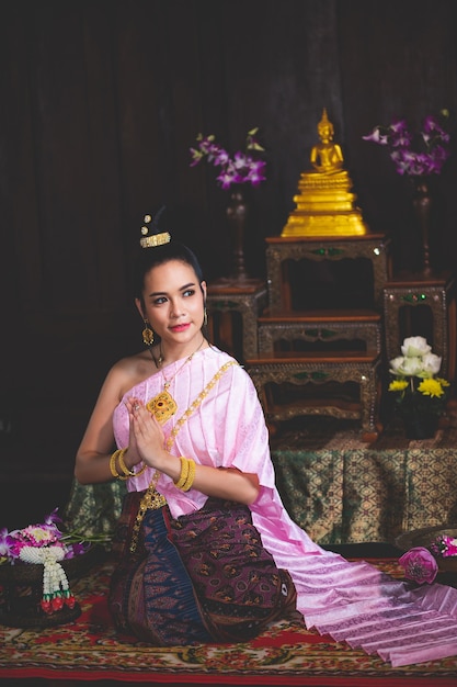 Foto hermosa mujer asiática, tailandeses llevaba un vestido retro tailandés rosa y descansaba las manos en la sala de oración.