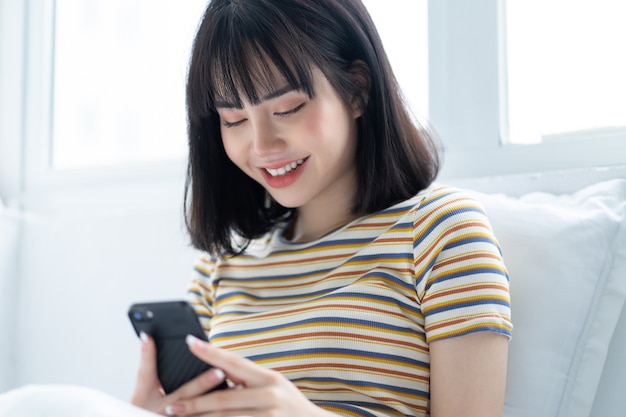 Hermosa mujer asiática con teléfono en la cama en el dormitorio