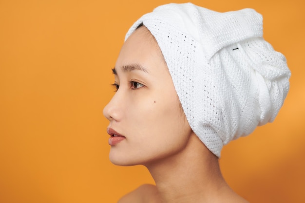 Hermosa mujer asiática con una toalla en la cabeza sobre fondo naranja. Concepto de belleza Spa.