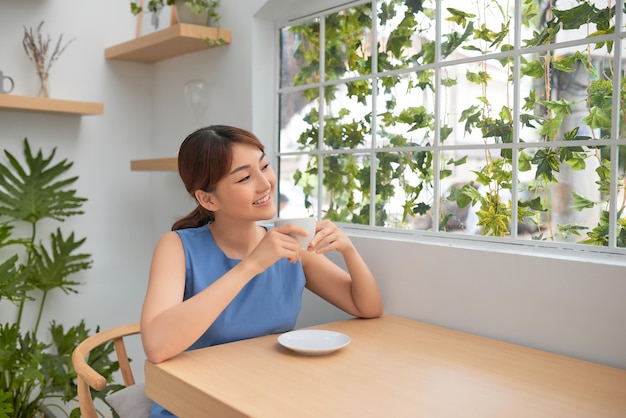 Hermosa mujer asiática tomando café detrás de la ventana verde