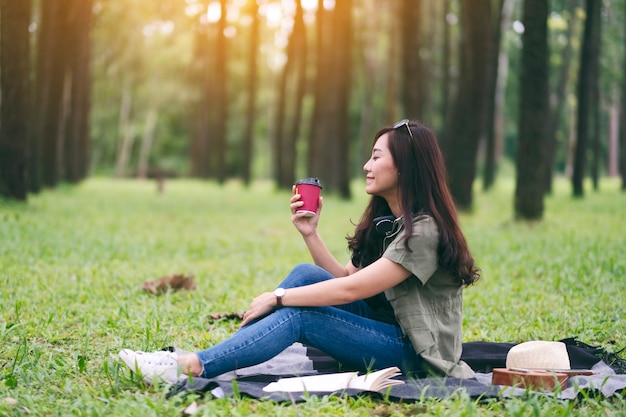 Una hermosa mujer asiática tomando café mientras está sentado en el parque
