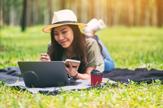 Una hermosa mujer asiática trabajando y escribiendo en la computadora portátil mientras está acostada en el parque