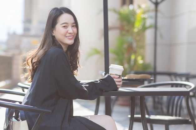 Hermosa mujer asiática en un traje azul oscuro está sentada en una silla sosteniendo una taza de café