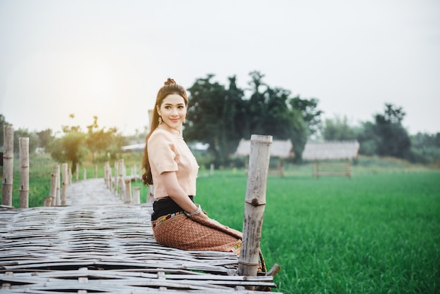 Hermosa mujer asiática en traje local sentado y disfrutar de natural en el puente de bambú en campo de arroz