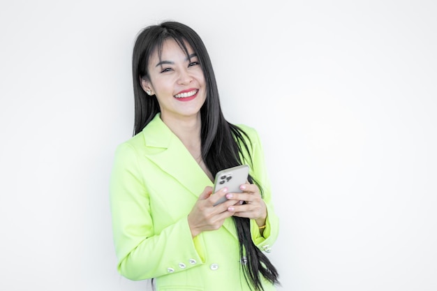 Hermosa mujer asiática en traje verde pastel usando teléfono inteligente gesticulando sí aislado sobre fondo blanco Feliz chica alegre con cabello largo celebrando la victoria mujer asiática exitosa en las redes sociales