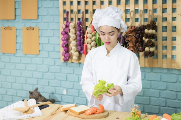 Una hermosa mujer asiática con uniforme de chef tailandés. Actualmente está preparando sándwiches en la cocina, preparando la cocina y preparando ideas.