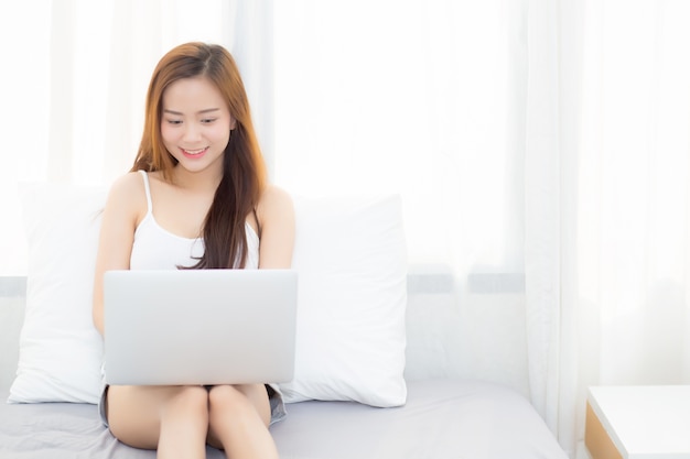 Hermosa mujer asiática usando la computadora portátil en el dormitorio.