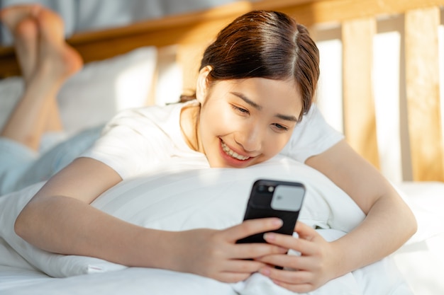 Hermosa mujer asiática usando su teléfono cuando se despierta