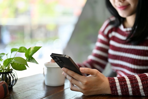 Hermosa mujer asiática usando su teléfono inteligente mientras se relaja en la cafetería imagen recortada