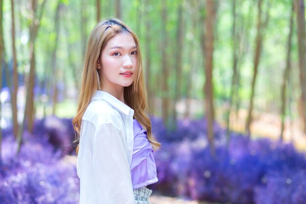 Hermosa mujer asiática vestida con camisa larga blanca sonríe alegremente y se encuentra en el jardín de flores púrpura