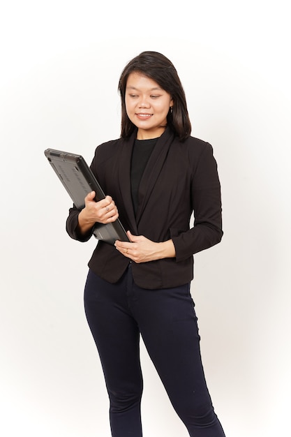 Hermosa mujer asiática vestida con traje negro sosteniendo portátil aislado sobre fondo blanco.