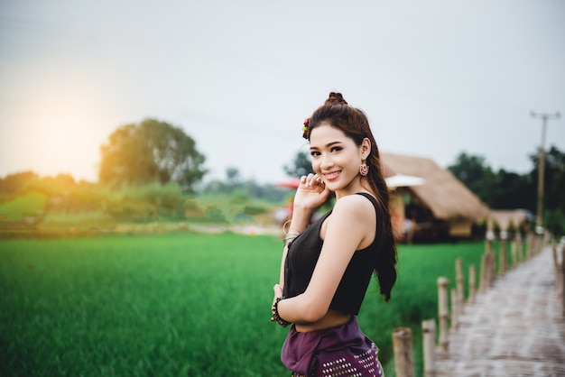 Hermosa mujer asiática en vestido local de pie y disfruta natural en el puente de bambú en el campo de arroz