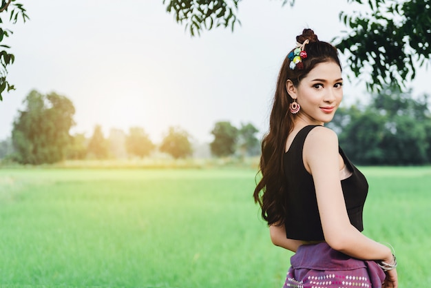 Hermosa mujer asiática en vestido local de pie y disfruta natural en el puente de bambú en el campo de arroz