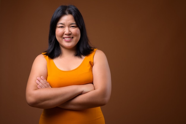 Hermosa mujer asiática con vestido sin mangas naranja sobre marrón