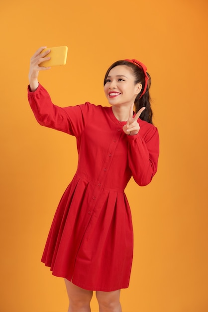 Hermosa mujer asiática con un vestido rojo y de pie sobre un fondo naranja