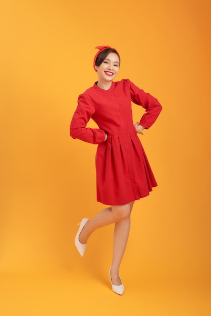 Hermosa mujer asiática con un vestido rojo y de pie sobre un fondo naranja