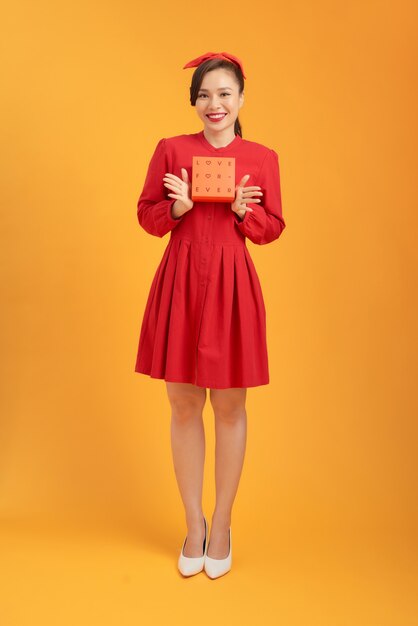 Hermosa mujer asiática con un vestido rojo y de pie sobre un fondo naranja