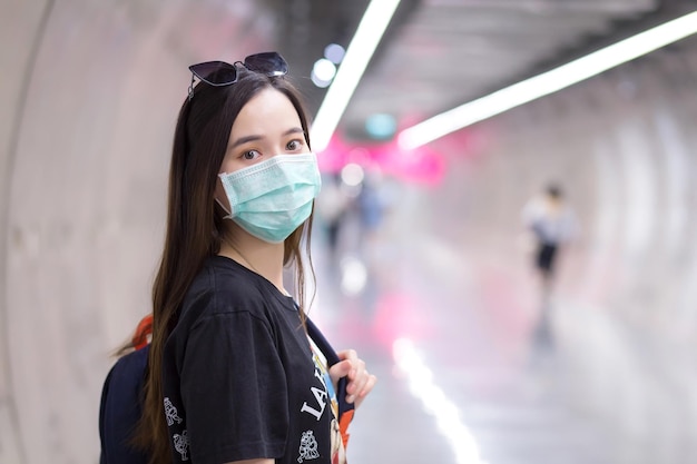 Hermosa mujer asiática viste camisa negra y mascarilla médica mientras camina hacia el túnel del metro