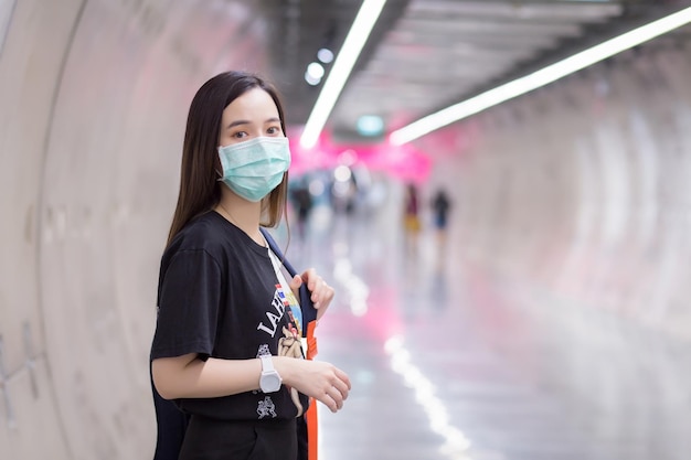 Hermosa mujer asiática viste camisa negra y mascarilla médica mientras camina hacia el túnel del metro