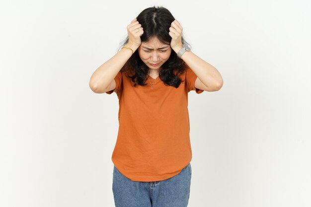 Foto hermosa mujer asiática vistiendo camiseta de color naranja con dolor de cabeza aislado sobre fondo blanco.