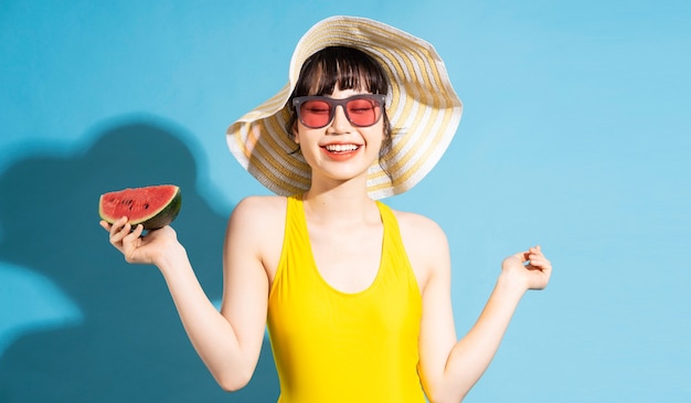 Hermosa mujer asiática vistiendo mono amarillo sobre azul y comiendo frutas tropicales