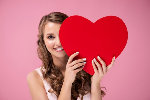 Hermosa mujer asoma detrás de un gran corazón rojo